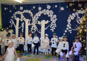 Dzieci z grupy Żabki, przebrane za śnieżynki i bałwanki, tańczą.